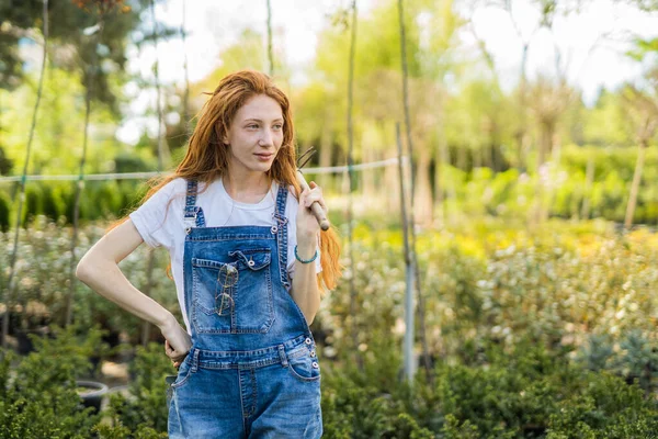 Stock image Lovely ginger gardener holding digger on shoulder and looking aside while standing at the garden. Copy space