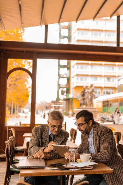 stock image Two senior businessmen are looking at the documents on the tablet while talking about them in the cafe