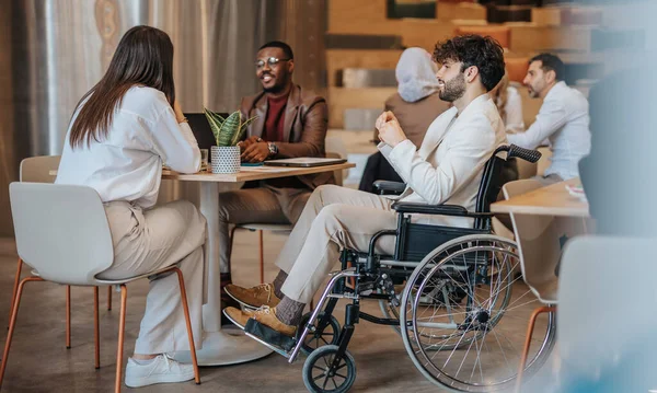一个坐在轮椅上的年轻英俊男子和他的同事一起坐在餐馆里谈论生意 — 图库照片