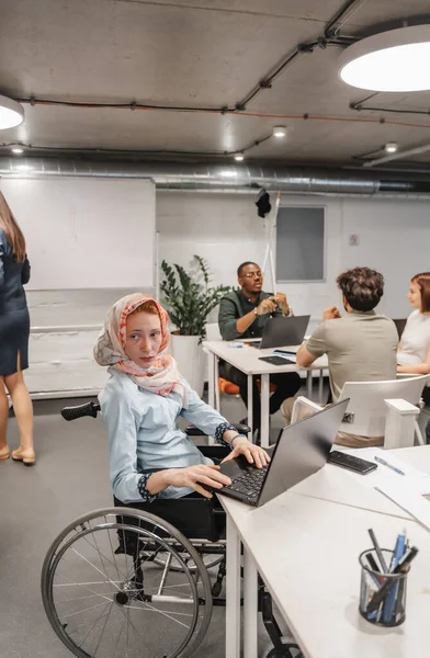 車椅子の麻痺したビジネスマンは 現代のオフィスルームでラップトップに取り組んでいる間 何かによって気を取られました — ストック写真