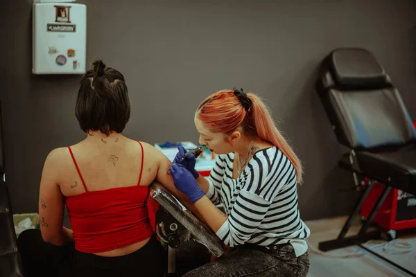 纹身师坐在工作室为她的客户纹身 — 图库照片