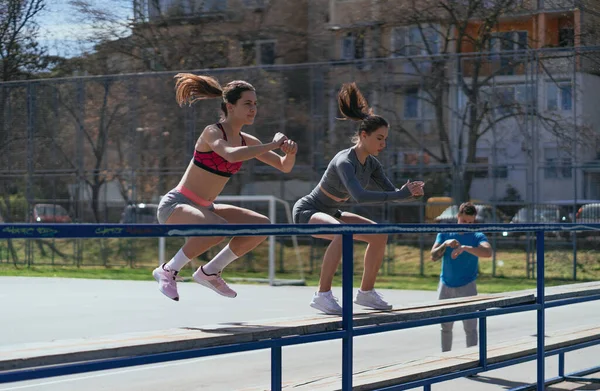 건강에 스포츠 여자들 벤치에서 점프를 다리를 운동하고 그들의 친구가 휴식을 — 스톡 사진
