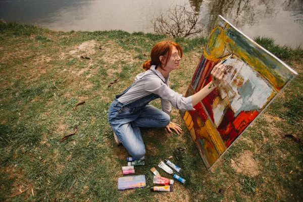 草の上に座っている間 大きなキャンバス上のパン絵の中に赤い髪の女の子 — ストック写真