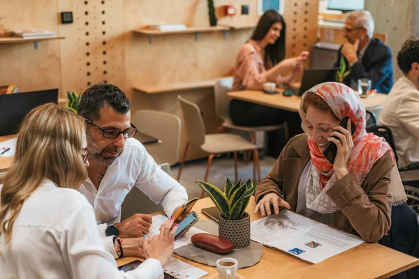 ヒジャーブを着たイスラム教徒の女性従業員は 電話をかけ プロジェクトの詳細を議論している彼女の中年の同僚に耳を傾ける — ストック写真