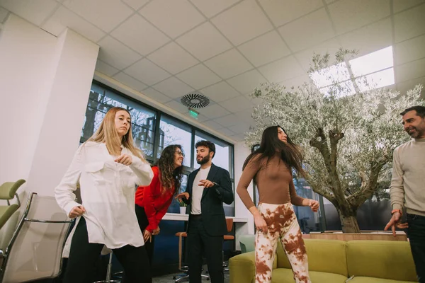 Creative international group of people dancing at the office after successful month at work. They are celebrating teamwork and project results. Dancing at the office