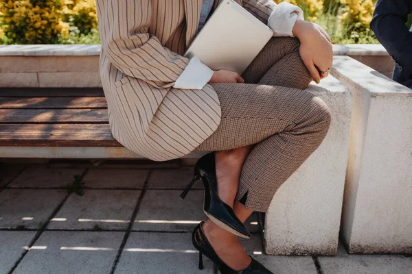 カジュアルなビジネス衣装とハイヒールのビジネスマンの写真は 屋外のベンチに座っている間 彼女の手でラップトップを保持しています — ストック写真