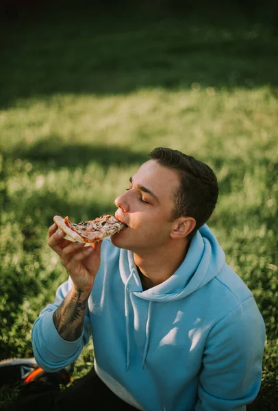 Snygg Pojke Äter Pizza Medan Han Sitter Gräset Parken — Stockfoto