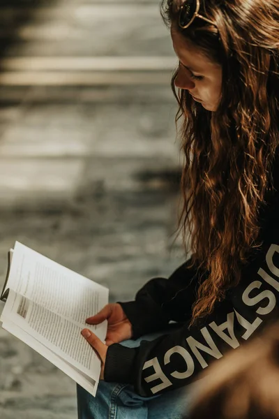 在城市的长椅上 一头金发的黑发女孩坐在那里看书 近距离拍摄 — 图库照片