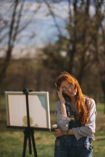公園に立っている間 彼女のキャンバスを見て考えて美しい生姜の女の子のクローズアップ — ストック写真