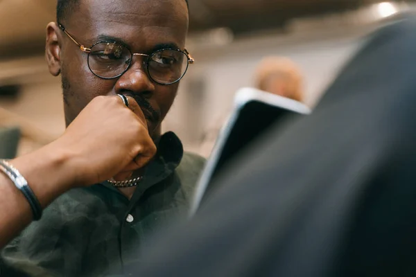 仕事でタブレットに取り組んでいる間深く考える眼鏡を身に着けている良い見た目の黒人男性の従業員の写真を閉じます ローアングルビュー — ストック写真