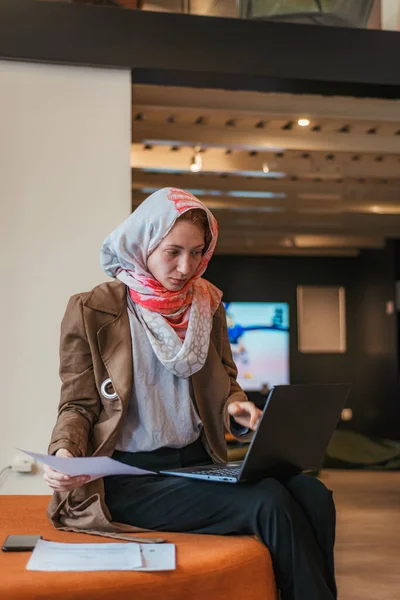 戴头巾的女雇员在共同工作的空间工作 使用膝上型计算机 做文书工作 看膝上型计算机 — 图库照片
