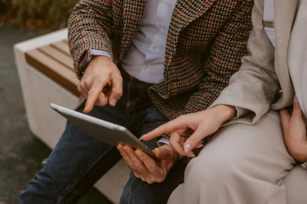 Close up og business colleagues pointing at the tablet while sitting on the wooden bench