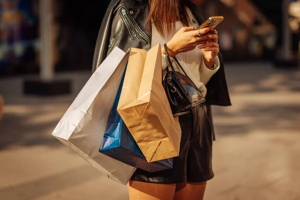 Female person with shopping bags on her armn is checking her phone