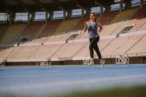 A lovely female sportsperson is running around the stadium, on a sports track, on a beautiful sunny day