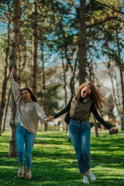 两个笑容可亲的漂亮姑娘在公园里散步时张开双臂 他们手牵着手 前视镜拍摄 — 图库照片