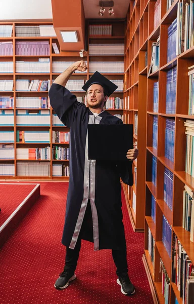 又兴奋又年轻的男子自豪地在图书馆里拿到了大学学位 — 图库照片