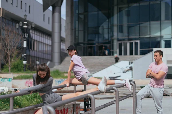 Młody Instruktor Fitness Obserwuje Swoje Dwie Klientki Ćwiczące Nogi Metalowym — Zdjęcie stockowe