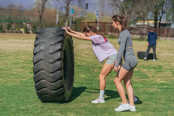 强壮的女孩在公园里锻炼 穿着粉色衬衫的女孩在翻动一个巨大的卡车轮胎 — 图库照片