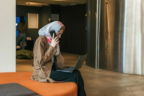 Kvinnlig Anställd Sitter Orange Soffa Med Telefonsamtal Medan Arbetar Laptop — Stockfoto