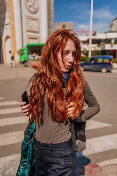 Female ginger tourist hanging out in the city with backpack on. She is looking at something