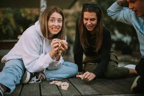 ブロンドの女の子の近くに彼女の友人と座っている間 彼女の手で木製のジャンガーを保持 — ストック写真
