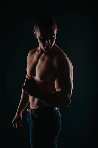 肌肉发达又有魅力的男人站在一间黑暗的房间里 伸展着他的肌肉 — 图库照片