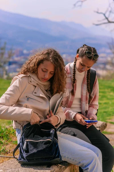 二人の女の子が屋外で宿題を書こうとしている 彼女の学校のバッグを開けるカーリーハイレッドガール — ストック写真