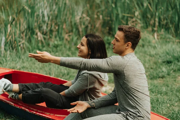 男の子が彼のガールフレンドに何かを示している間 公園の赤いカヤックに座っている美しいカップル — ストック写真
