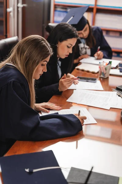 一群年轻的大学生 穿着礼服 签了名 并在书桌上填写文件 — 图库照片