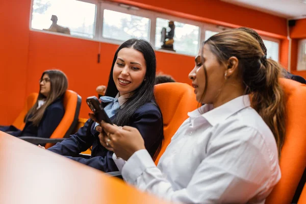 2人の女性学生が話し 笑顔で 教室で電話を見ている — ストック写真