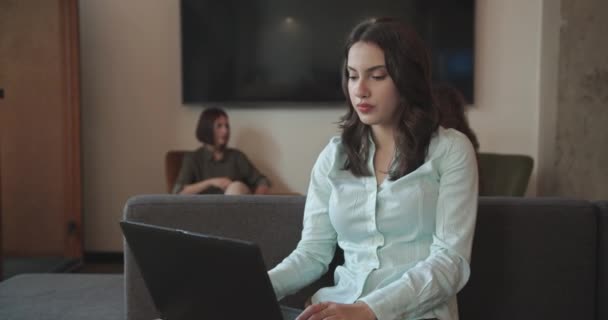 在沙发上休息的时候 漂亮的年轻女性在笔记本电脑上工作 同事们在办公室的咖啡厅里讨论着她的商业理念 还有相机卡车司机 — 图库视频影像