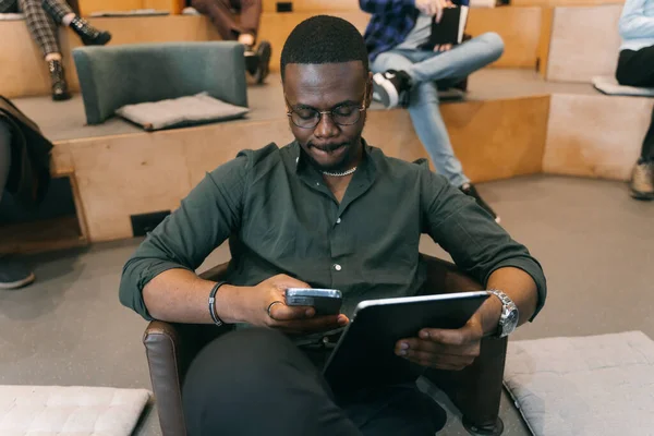 タブレットで作業中に携帯電話をチェックしているハンサムな黒人男性のフロントビュー写真 — ストック写真