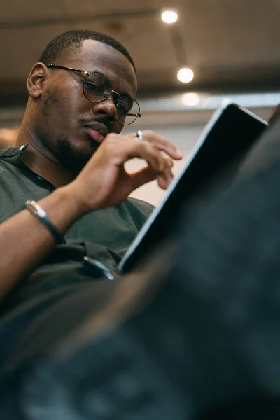 Good looking black male person working on tablet. Low angle view photo