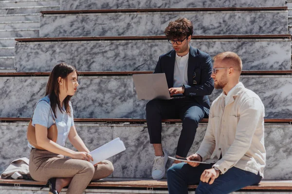 Young, beautiful business partners discussing during meeting outdoors sitting on stairs in the downtown area