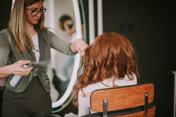 Hair stylist spraying female ginger client hair at the salon