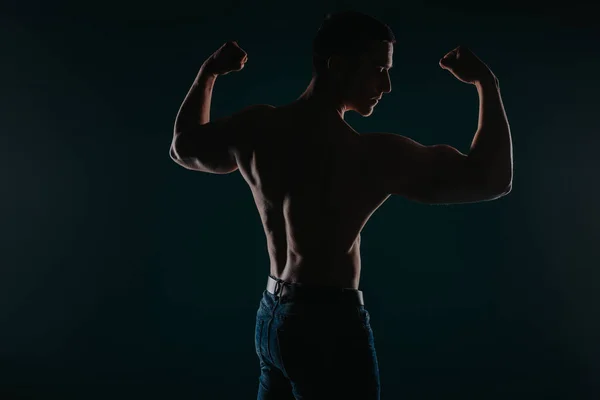 Well-built and charming man standing in front of a dark background and flexing his arms