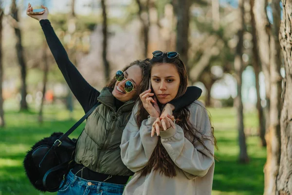 两个女孩在公园里 布鲁内特女孩有一个电话 卷发女孩拥抱着她 — 图库照片