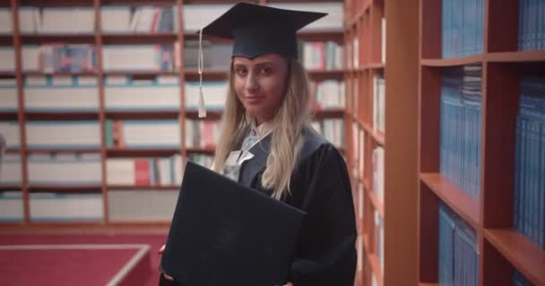 在图书馆骄傲地拿着毕业文凭 证明大学毕业后就能获得毕业文凭的学生 — 图库视频影像