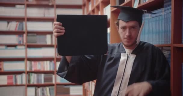 在图书馆骄傲地拿着毕业文凭的大学生 可以在大学毕业后获得毕业证书 — 图库视频影像