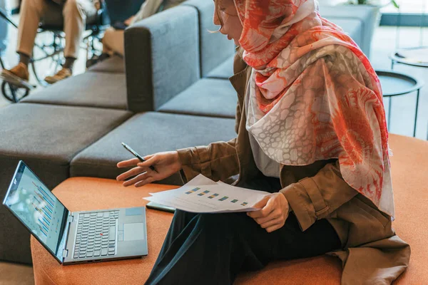 Kobieta Hidżabie Analizuje Dane Wykresy Siedząc Kanapie Biurze — Zdjęcie stockowe