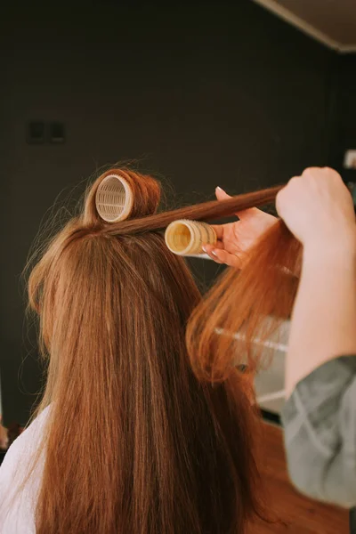 Close up of hairdresser putting hair rollers on her clients red hair at the salon