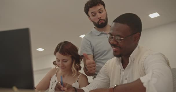若い白人女性と若い黒人男性とシニアマネージャーが加わったプロジェクトでオフィスで一緒に働いていました オフィスのポジティブな精神 調和と寛容さを象徴する — ストック動画