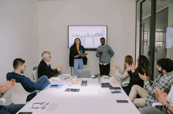 Multiracial business partners explaining charts on the presentation monitor. Smiley brunette woman looking at the camera