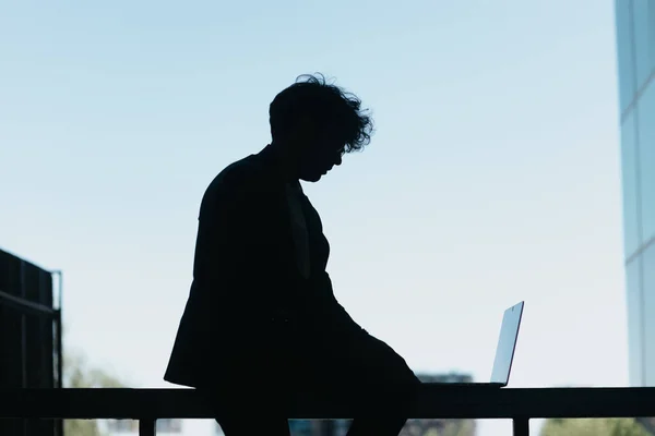 Mann Sitzt Mit Laptop Auf Einem Metallzaun Silhouettenfoto — Stockfoto