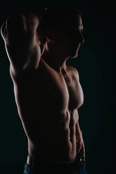 Stunning and well-built man standing in a dark room and flexing his upper body