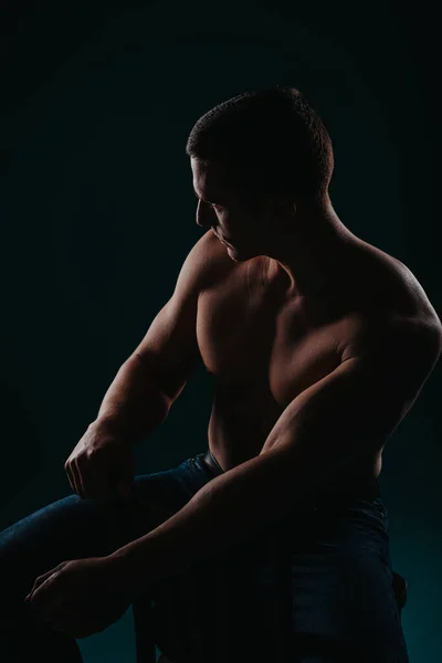 Jonge Shirtloze Bodybuilder Poserend Studio Zittend Een Stoel Opzij Kijkend — Stockfoto