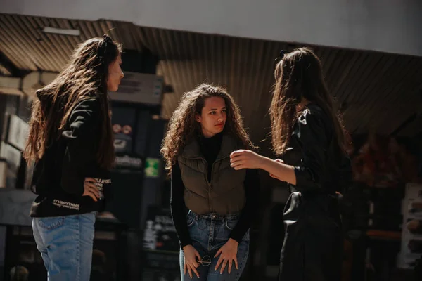 Girl in black coat telling a story to her friends while hanging out. Her curly haired friend cannot believe what is hearing