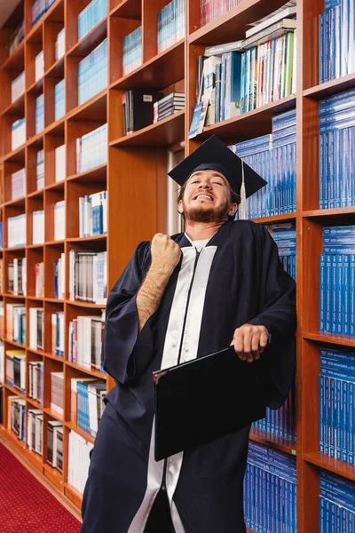 Genç Mezun Kep Cübbesini Takmış Üniversite Diplomasını Alıp Kütüphane Raflarında — Stok fotoğraf