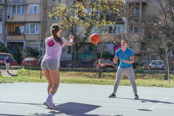 Handsome male sports person teaching his female friend how to pass basketball ball