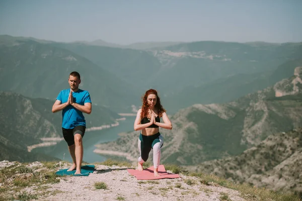 Yoga couple making yoga  poses on the yoga mats at the top of the mountain